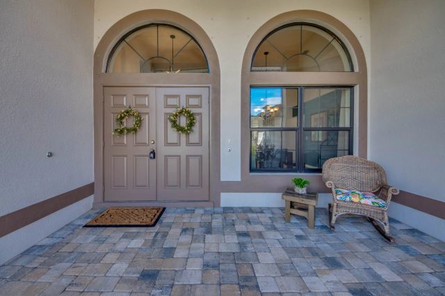 Double front door with two wreaths and arched windows, a wicker chair in front