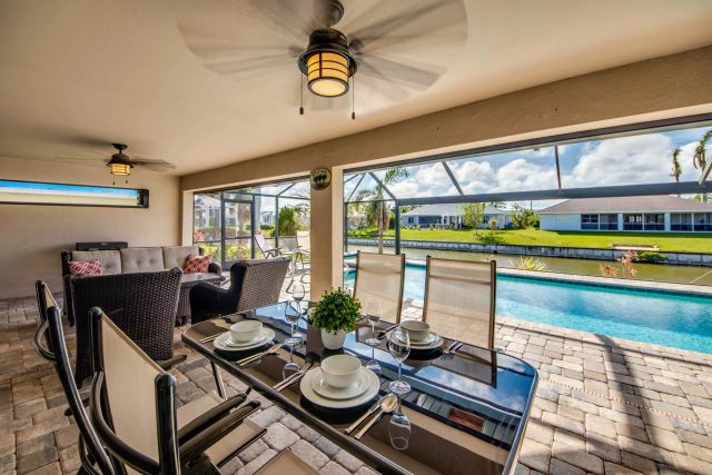 Dining table under the lanai roof with a ceiling fan, the pool on the right
