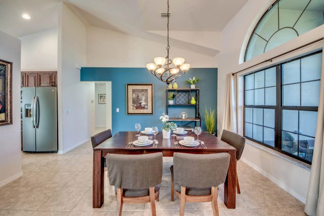 Set dining table with chairs under a chandelier, a stainless-steel fridge on the left