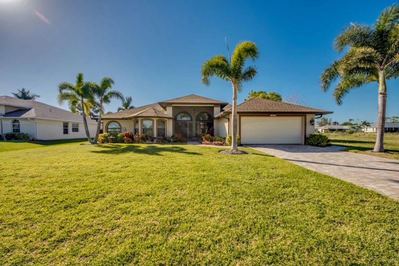 Front of the villa with garage, lawn and palm trees under a blue sky