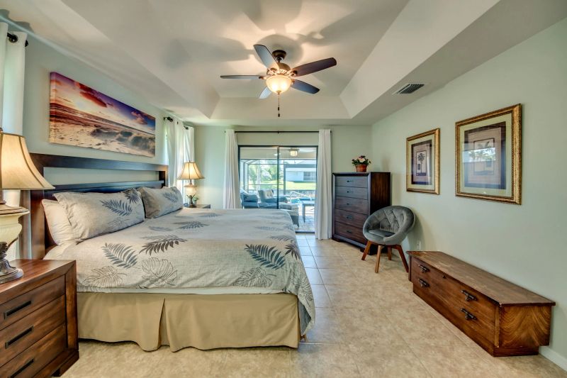Master bedroom with a large bed, ceiling fan, chest at the foot of the bed and a sliding door