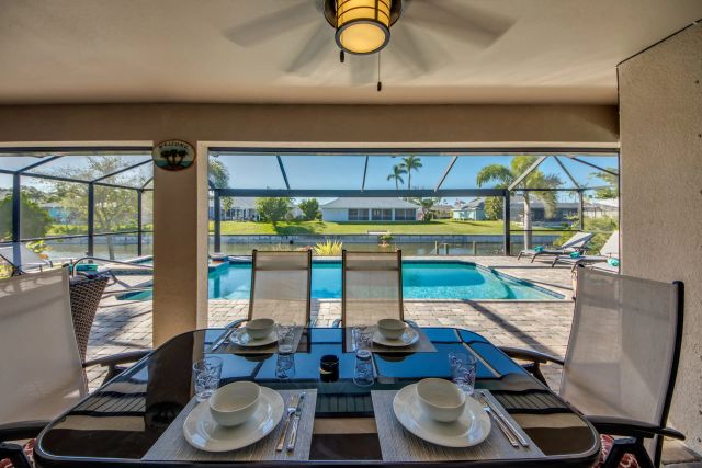 Set dining table on the covered lanai, with the pool and canal behind