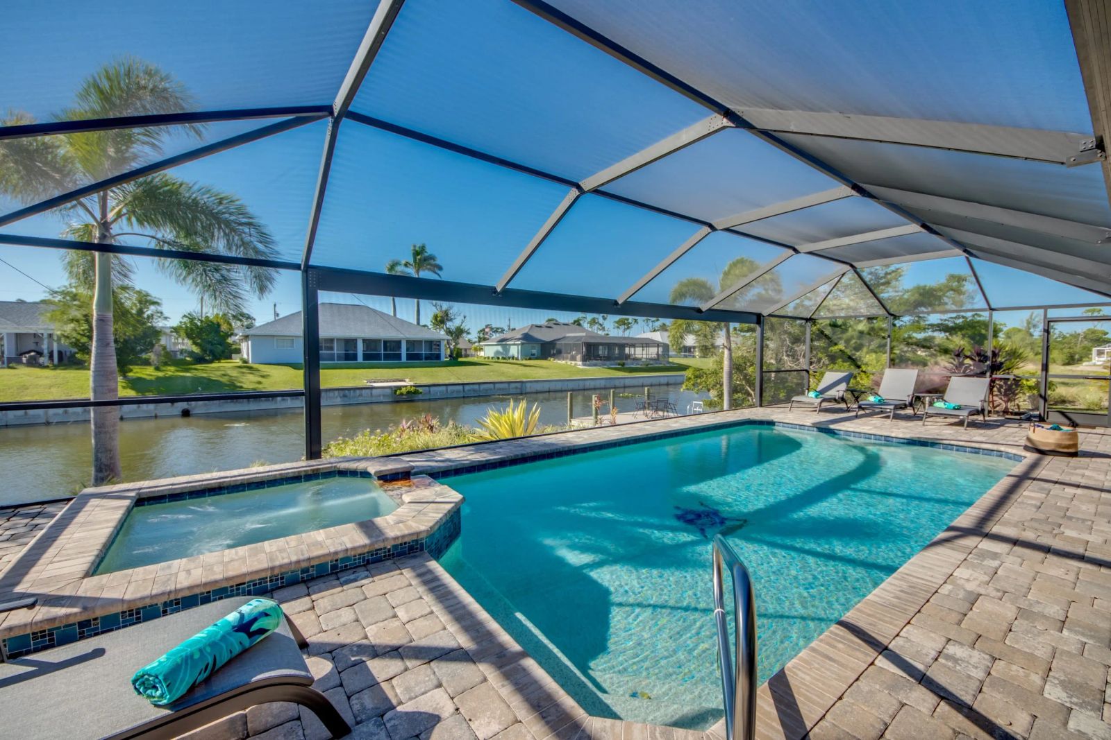 Pool with an adjoining spa inside the screen enclosure, loungers on the right and the canal beyond