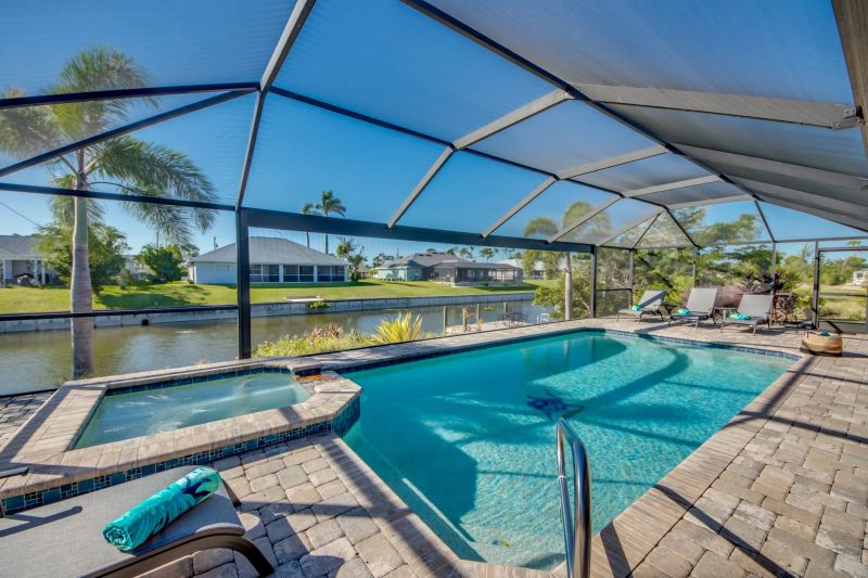 Pool with an adjoining spa inside the screen enclosure, loungers on the right and the canal beyond