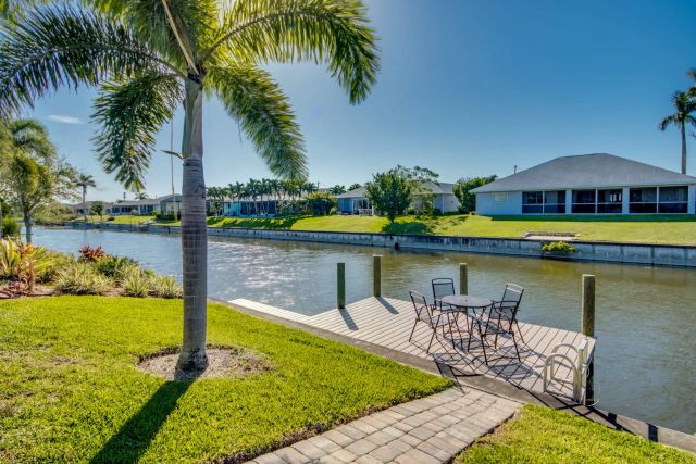 Lawn with a palm tree and a dock with table and chairs beside the canal